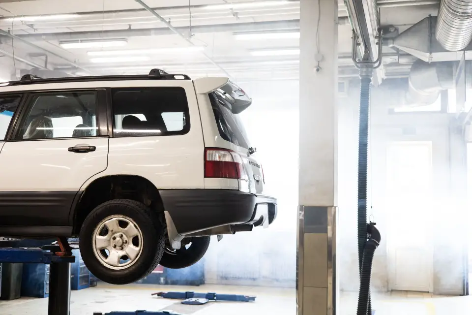 A white SUV raised on a lift in a bright garage workshop, ready for a service