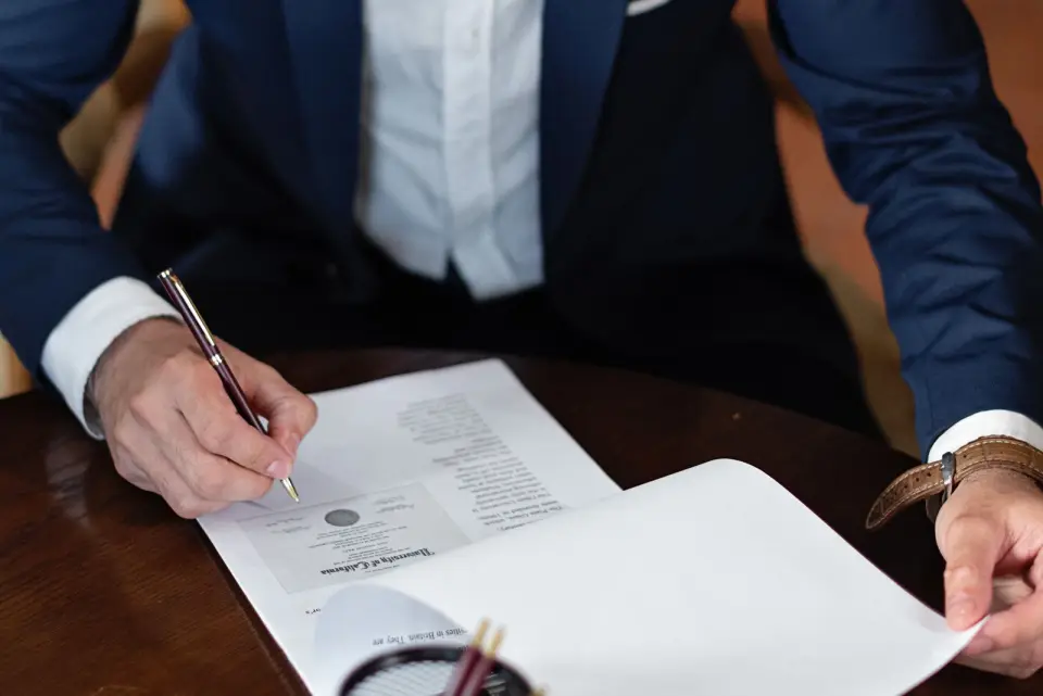 A solicitor reading and signing a printed document at a wooden desk