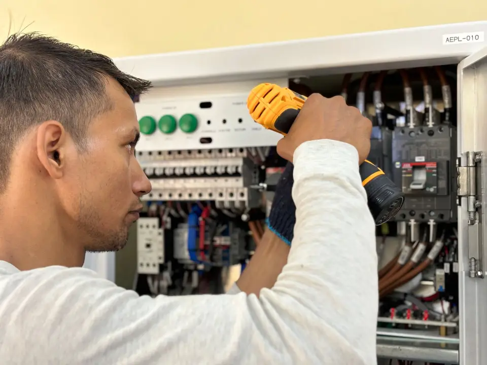 An electrician using a drill on the wiring of an open fuse board